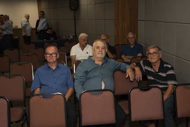 Três associados sentados na fileira do auditório posam para a foto antes do início da cerimônia.