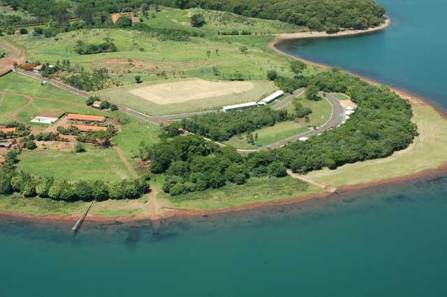 Vista aérea da península da pousada cercada pela represa, com o campo de futebol e os alojamentos.